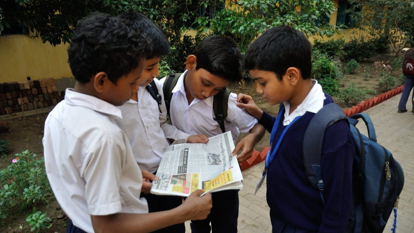 A group of students sitting together and reading a newspaper spread open between them