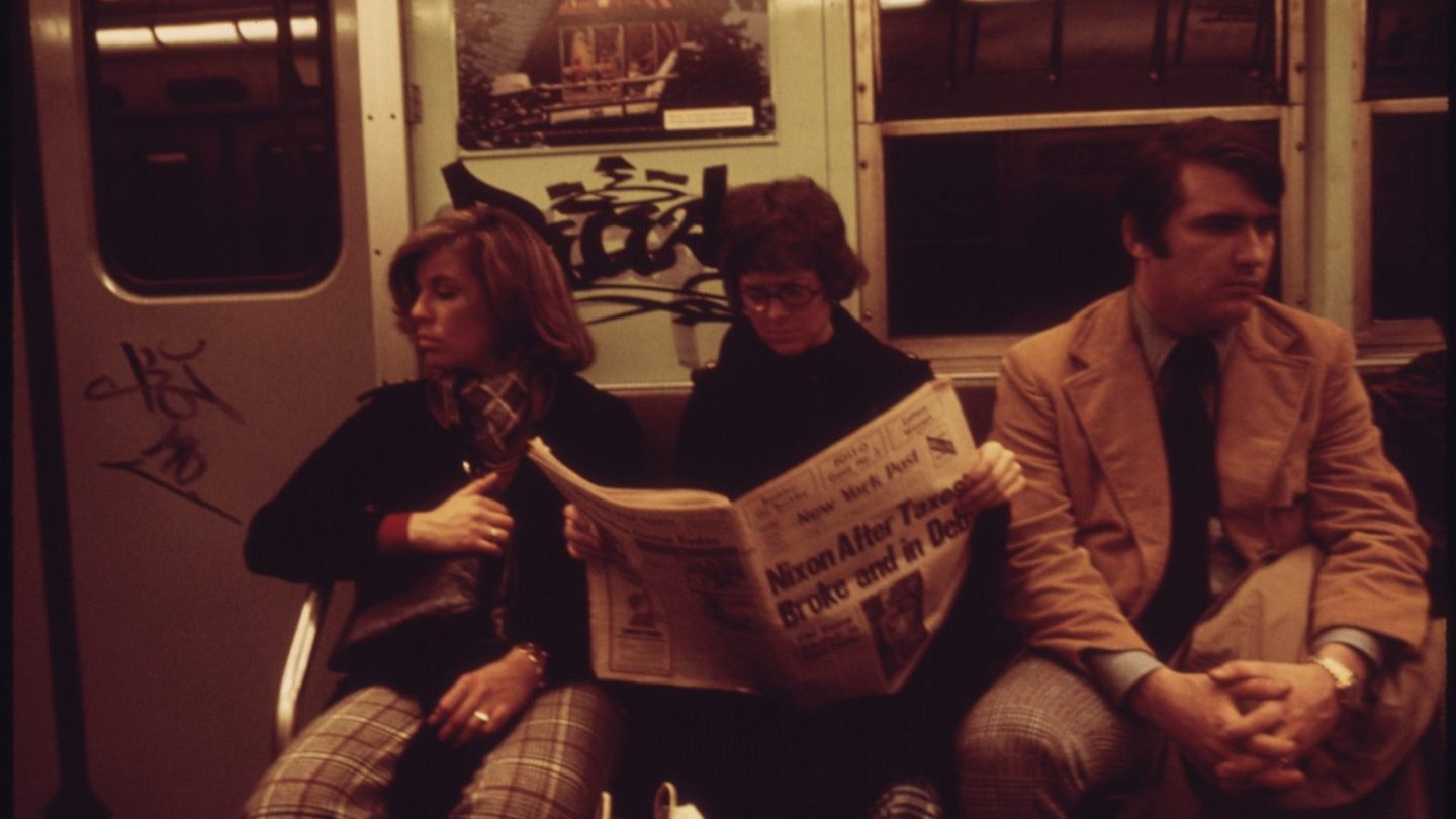 Passengers on a New York City subway car in 1974, one reading a newspaper with a Nixon headline on the front page